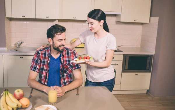 Güzel giel adam duruyor ve plaka Anadolu ve kiraz domates ile verin. O ve gülümseme inceliyor. Adam acıkmış. Masada oturuyor. Orada meyve ve bardak suyu.