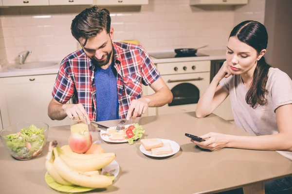 Mutlu adam oturur ve masa ve omlet yiyor. Bıçak ve çatal ile o parçalar halinde gıda keser. Kız o elinde tutan telefon bakar. Bıkkın ve yorgun bir kız. — Stok fotoğraf