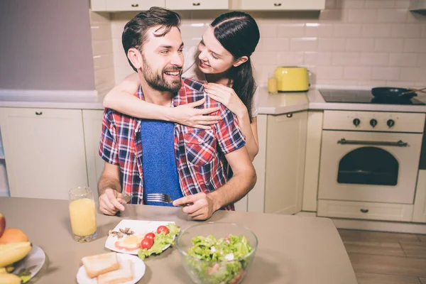 Adam oturur ve tablo ve yiyor gıda şirin resmi. O kız ve gülümsüyor görünüyor. Kadın onun arkasında duruyor ve adam embrace. Mutlu görünüyorlar. — Stok fotoğraf