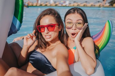 Seksi ve güzel modelleri yüzme havuzunda beyaz kayan nokta üzerinde durur. Onlar ve kameraya poz. İlk kız sıcak görünüyor. İkinci bir hayran. Onlar dinlen.