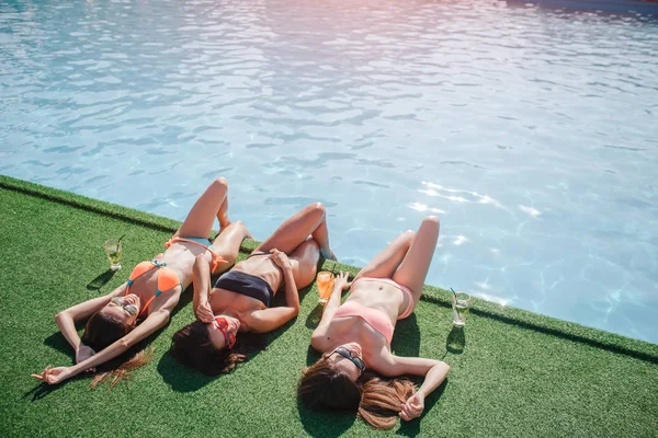 Tři modely jsou leží na trávě. Oni drží nohy ve vodě a získat opálení od slunce. Modely stratching a spánkem. Jsou to uvolněný a klidný. — Stock fotografie