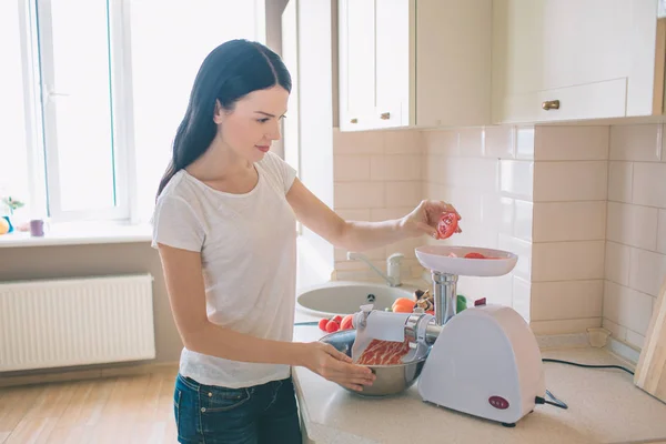 Kadın resim standları ve domates kıyma makinesi yukarıda parça tutar. O kase forcemeat ile tutar. Ciddi ve yoğun bir kadındır. — Stok fotoğraf