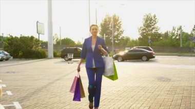 Mutlu ve kendine güvenen iş kadını sokakta yürür ve shoopping torba tutar. Çok güzel ve kendinden emin görünüyor. Kız mavi takım elbise giyiyor.