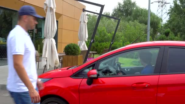 Girl drives car. She stopped and came out of it. Guy comes to red car. She gives him keys and walk away. Man sits down in car and ride on it. — Stock Video