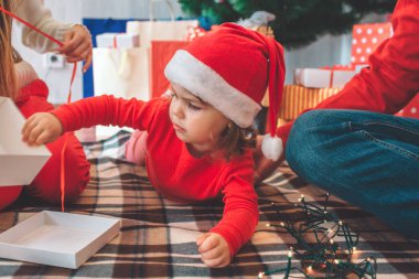 Mutlu Noeller ve mutlu yeni yıl. Battaniye yüzüstü yatarken çocuk resmi. Kız Beyaz kutunun dokunmuyor. Yetişkin bu tutar. Adam onun sağ tarafında. Anne kırmızı kurdele tutar.