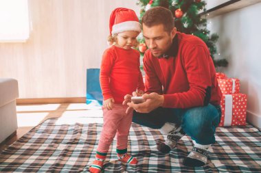 Mutlu Noeller ve mutlu yeni yıl. Baba ve kızı birlikte bekletin. Üst tutuşsun cep telefonu. Gadget görünüyorlar. Ciddi ve konsantre insanlar.