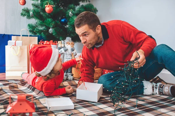 Joyeux Noël et bonne année. Jolie photo de parent et enfant sur couverture. La fille est allongée sur le ventre. Regarde le gamin et tiens les lumières de Noël. Ils s'assoient ensemble . — Photo