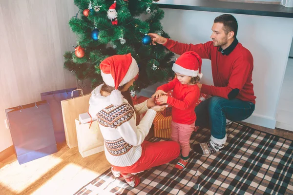 Joyeux Noël et bonne année. Image attrayante de la famille mignonne et agréable. Ils décorent l'arbre de Noël. Jeune femme tient jouet avec petite fille. L'homme met jouet bleu sur l'arbre . — Photo