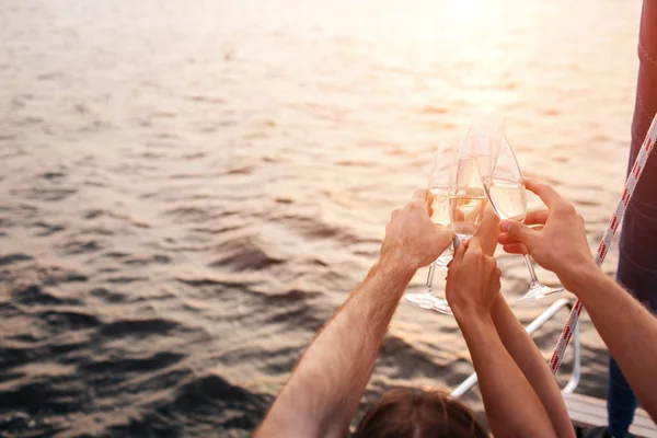 Bonita foto de cuatro manos sosteniendo vasos de champaigne frente al agua. Descansan un poco. Se pone más oscuro. El sol se pone . — Foto de Stock