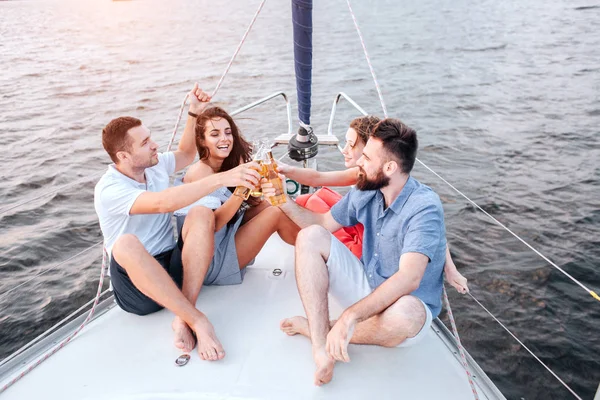 Brunette is smiling. Man on left hold hand on rope. Other tow people are smiling. Men keeps legs crossed.