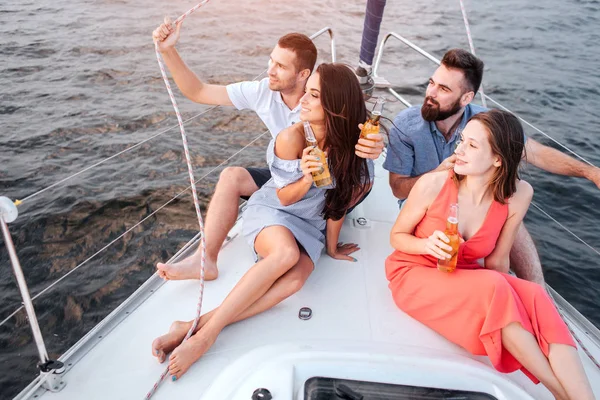 Zwei Paare sitzen auf dem Bug der Jacht. schauen sie nach links. Frauen werden exzidiert. Auch Männer sind glücklich. sie beobachten den Sonnenuntergang. — Stockfoto