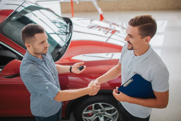 Gli uomini seri si alzano e si stringono la mano. L'acquirente ha le chiavi della macchina. Compresse a tenuta stagna. Hanno fatto un patto. La macchina rossa appartiene agli uomini a sinistra. . — Foto Stock