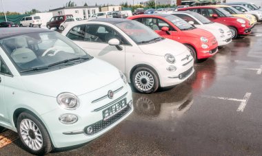 Küçük ve güzel fiat otomobil park yerinde ayakta dışında resmi. Kırmızı ve beyaz araba var. Asfalt tekerlekleri altında ıslak.