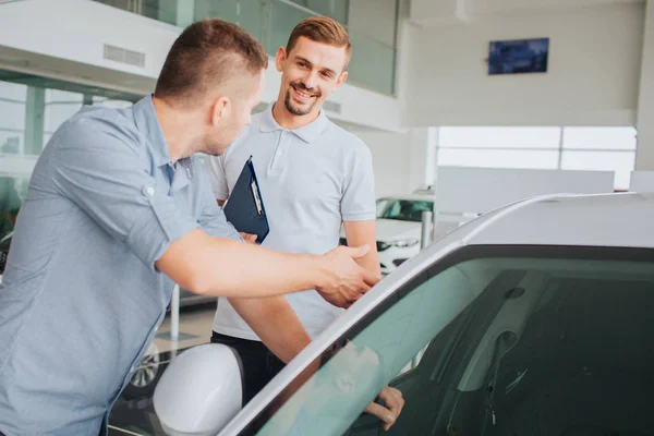 Olumlu ve sakallı genç satıcı müşteri önünde stand ve ona bakar. Gülümsüyor. Alıcı araba dokunur ve satıcı görünüyor. Cidden konuşuyor. — Stok fotoğraf