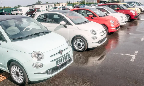 Picture of small and beutiful fiat cars standing outside on parking lot. There are red and white cars. Asphalt is wet underneath wheels. — Stock Photo, Image