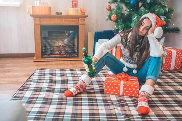 Mujer joven se sienta en el suelo y duerme. Ella tiene una botella verde de alcohol en la mano. Hay una caja con regalo entre sus piernas. Está borracha. . — Foto de Stock