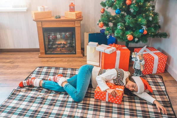 Photo d'une jeune femme couchée sur le sol et dormant. Elle est fatiguée mais heureuse. Brunette sourit un peu. Elle tient la main sur la boîte avec le cadeau . — Photo