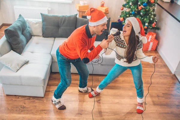 Emotional couple standing and singing together using microphone. They look at each other. People singing out loud. They wear Christmas clothes.