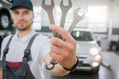 Yakışıklı delikanlı anahtarları kümesi gösterir. Onlara bakıyor ve gülümse. Adam üniforma giyer. Beyaz arabanın önünde durduğunu. Biraz gülümser genç adam.