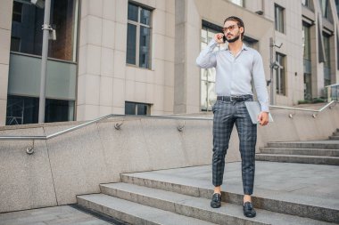 Ciddi ve conentrated şık işadamı standları ve teşkil etmektedir. O dizüstü el ve telefonuna kulak yakınsanız tutar. Yalındır görünüyor.