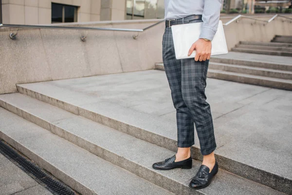 Geschnittene Ansicht des stilvollen Mannes stehen und posieren. Er hält Laptop in der Hand. Junger Mann steht auf Stufen. — Stockfoto