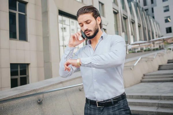 Le jeune homme d'affaires est très occupé. Il regarde des montres sur sa main. Le barbu parle aussi au téléphone. Il court sur les marches . — Photo