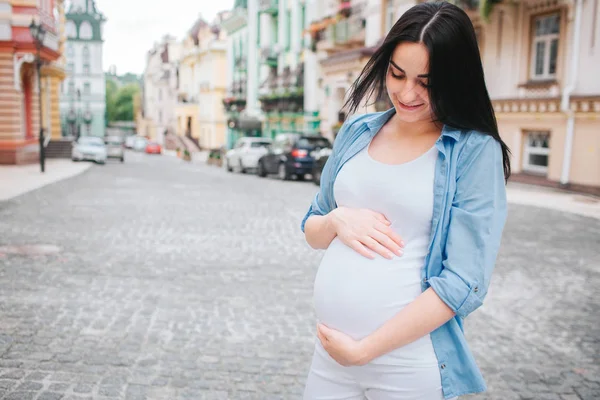 Portret szczęśliwy czarne włosy i dumni, że kobieta w ciąży w mieście w tle. Zdjęcie modelu kobiece, dotykając jej brzuch rękami. — Zdjęcie stockowe