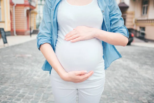 Portret szczęśliwy czarne włosy i dumni, że kobieta w ciąży w mieście w tle. Szczelnie-do góry obraz kobiet modelu dotykając jej brzuch rękami — Zdjęcie stockowe