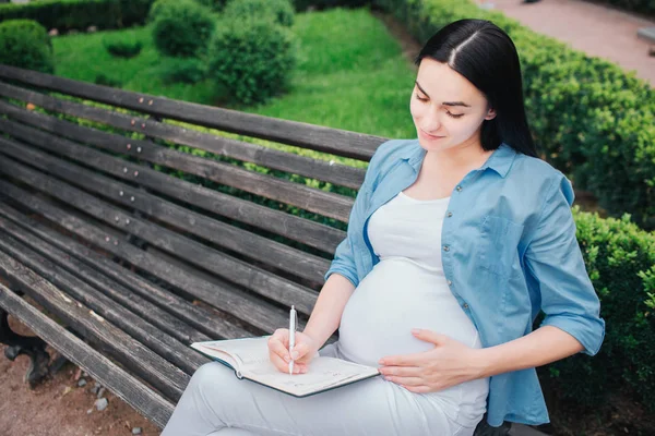 Portret szczęśliwy czarne włosy i dumni, że kobieta w ciąży w mieście w tle. Kobiece modelu jest Pisanie notatek do notesu. — Zdjęcie stockowe