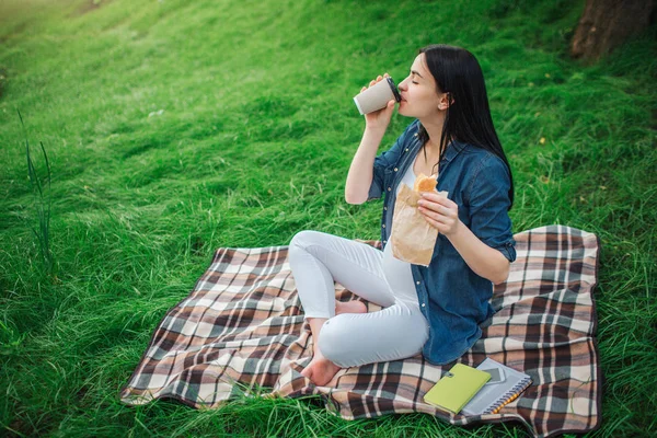 Portret szczęśliwy czarne włosy i dumni, że kobieta w ciąży, w mieście, w parku. Zdjęcie modelu kobiece, dotykając jej brzuch rękami. Siedzi na trawie i picia kawy lub herbaty kobieta model. — Zdjęcie stockowe