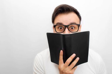 Erkek esmer kameraya bakarak resim. O kara kitap elinde tutar. O Offtime gözlük. Genç adam heyecanlandı. Beyaz backgorund izole.