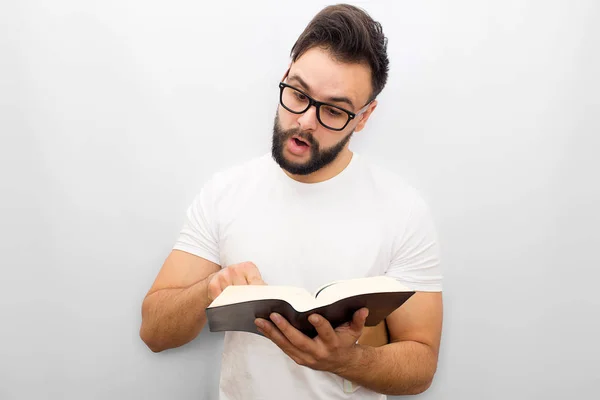 Foto di un giovane che legge ad alta voce dal libro. Lo tiene in mano e lo indica. Il giovane è concentrato. Isolato su sfondo bianco . — Foto Stock