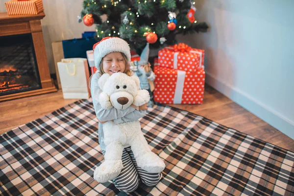 Szczęśliwy i pozytywne dziewczyna siedzi na koc na podłodze i embacing biały zabawka. Uśmiecha się. Dziewczyna wygląda szczęśliwy. Ona w pokoju sam. — Zdjęcie stockowe