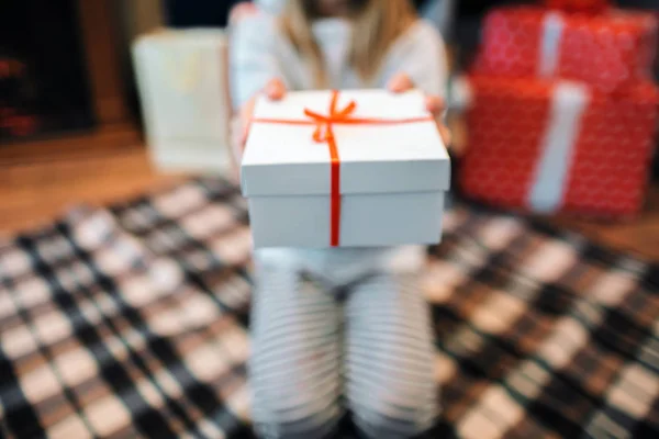 Corte la vista de la niña sentada en las rodillas y sosteniendo la caja blanca con presente. Hay cinta roja en ella. Ella lo sostiene con ambas manos . — Foto de Stock