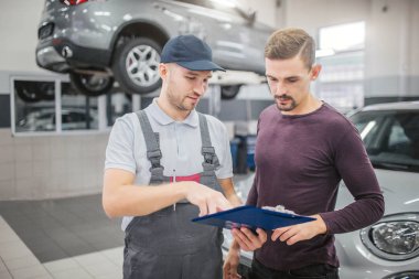 İki genç ve ciddi adam birlikte garajda bekletin. Plastik tablet belgeleri ile tutuyorlar. Onlara tek tip puan adam. Onlar ciddi ve yoğun bak. İşte araba arkalarında platformunda.