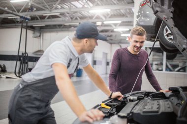 İşçi ve arabanın sahibi araç açık açık vücut dur. Sakallı adam bak. Alt araba için eğilir. Sahibi görünüyor. Garajda olduklarını.