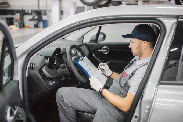 Un trabajador seguro se sienta en el auto y firma papeles. Los tiene en una carpeta de plástico. El coche está abierto . — Foto de Stock