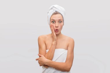 Güzel ve merak genç çilli kadın standları ve kamera üzerinde pozlar. Heyecanlandı. Onun vücut ve saç beyaz havlu ile kaplıdır. Gri arka plan üzerinde izole.