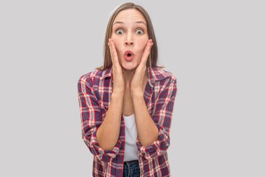 Güzel ve heyecanlı genç kadın anlamına gelir ve kamera üzerinde görünüyor. O wonderes. Modeli yanaklarda ellerini tutar. O beyaz t-shirt ve çello gömlek giyer. Gri arka plan üzerinde izole.