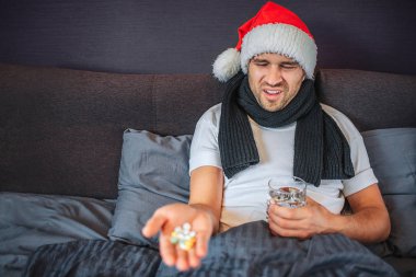 Genç adam yatakta oturur ve hapları el üstünde tutar. Onlara bakıyor ve küçülür. Adam kullanmak istemiyor onları yuttun. O su tutar. Onun boyun ve Noel şapka kafasına eşarp vardır.