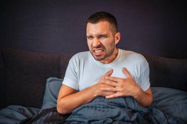 Genç adam ısı saldırı uğrar. Orayı üzerinde ellerini tutar. O küçülür. Genç adam kendini çok kötü hissediyor. Kapalı düşük uzuv / organ ile yatakta oturuyor.