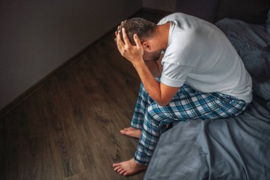 Yatak ve beklemeler kenarında oturan genç adam resmini ellerinizi başınızın koyun. Baş ağrısı vardır. Adam acı hissetmiyor. O uğrar.
