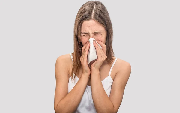 Mujer enferma y enferma estornudando en servilleta seca. Mantiene los ojos cerrados. Sufrimiento modelo. Aislado sobre fondo gris . — Foto de Stock