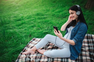 Bir mutlu siyah saç ve arka planda bir şehirde gurur hamile kadın portresi. Bir şehir bankta oturuyor. Bekleyen anne ile doğmamış bir çocuk parkta müzik dinleme