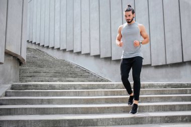 Genç adam koşu. O merdivenlerde aşağı çalışır. Kas ve su kuyusu-yapılı bir adam ciddi ve konsantre. Spor üniforma giyiyor.