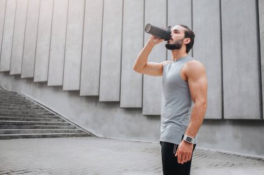 Kaslı ve su kuyusu-yapılı genç adam anlamına gelir ve siyah şişe suyu içer. O arama yapar. Adam beton duvarlar yakın duruyor.