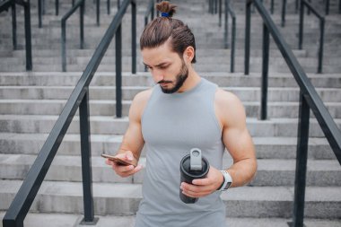 Merdiven ciddi ve kaslı bir genç adam durur ve bakar o hs bir elinde telefon. Bir tane de siyah şişe vardır. O sakin ve konsantre..