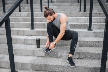 Sporcu geri kalan adımları vardır. Orada oturup, Ayakkabı bağcıklarımı bağla. Genç adam aşağı görünüyor. O su kuyusu-yapılı ve iyi şekil üzerinde.