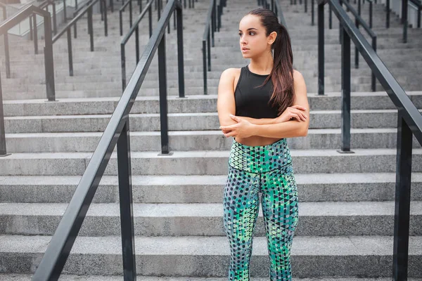 Imagen de una joven fuerte y bien construida se para en las escaleras y mira a la izquierda. Ella posa en cámara. Modelo lleva un buen uniforme deportivo. Ella está sola. . —  Fotos de Stock