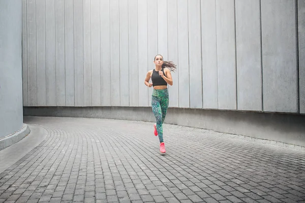 Imagen de una joven deportista corriendo por el pasillo. Lo hace muy rápido. La modelo corre sola. Ella saluda con sus manos . —  Fotos de Stock